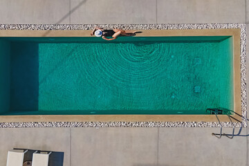 Woman sunbathing on the edge of the swimming pool in luxury villa or hotel. Aerial drone view