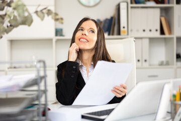 Positive woman bookkeeper doing paperwork during workday in office.