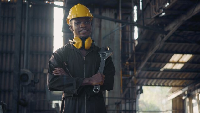 Portrait American Industrial Black Young Worker Man Smiling With Yellow Helmet In Front Machine, Engineer Standing Holding Wrench Tools And Arms Crossed At Work In The Industry Factory.