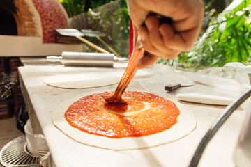 Fresh Italian pizza making process with hand of chef put tomato sauce on dough and pizza