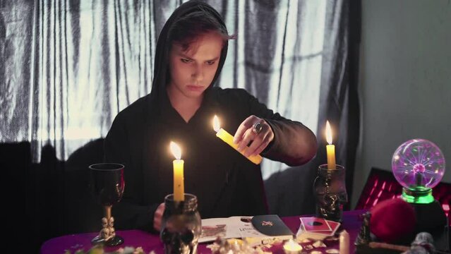 Male fortune teller psychic holding a magic pendulum over a candle and looks at photo with lost person