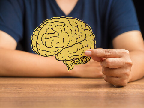 Man in a casual holding a brain shape made from yellow paper while sitting at the table