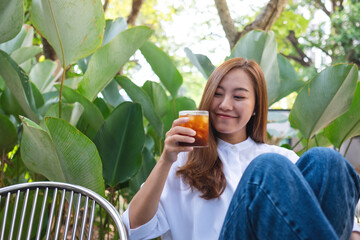 Portrait image a young asian woman holding and drinking iced coffee in the outdoors cafe