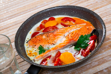 Close up of fried scrambled eggs and with salmon and tomatoes on fry pan