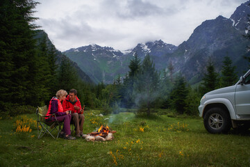 Couple chatting by bonfire in a camping in a dark mountain valley. White car. - 498663067