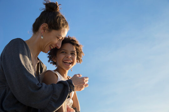 Mother and mixed race adopted daughter enjoying a leisure time and laughing together outdoors at sunset time during summer vacation. Family love concept. Mother's day. Copy space