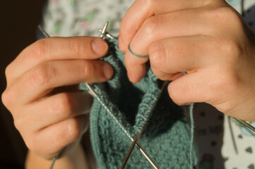 Close-up hand knitting. Hobbies, handicrafts. Knitting warm clothes from woolen fine yarn by hand on metal needles. Selective focus