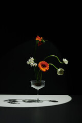 Vertical creative still life composition of fresh flowers in coupe glass on gray table surface...