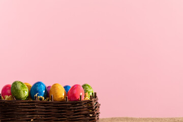 Wicker basket with Easter eggs stands on linen fabric. Easter.