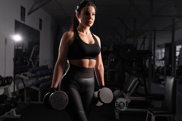 Fototapeta na wymiar Determined woman loses weight in the gym and trains with dumbbells. concept of sports and recreation. Beautiful woman in sportswear with heavy dumbbells in her hands.