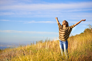 Fototapeta premium The hills are alive. Shot of an attractive young woman standing in a field on a hillside with her arms in the air.