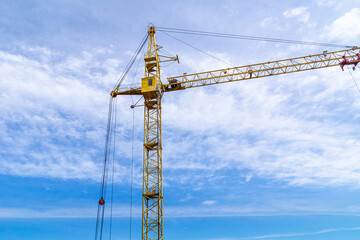 Yellow construction tower crane works against a bright blue sky