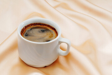 Cup of black coffee on wavy gold colored satin fabric with copy space