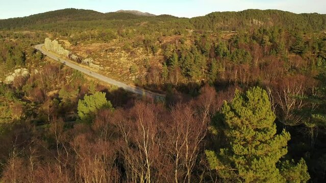 flying over a hill in norwegian landscape exposing a lonely road with a lonely rider