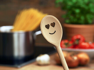wooden cooking spoon with heart smiley in front of saucepan with spaghetti and other ingredients...