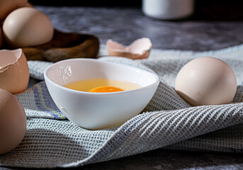 Fototapeta na wymiar A broken raw chicken egg in a white cup on a towel on a gray marble background
