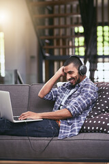 Thats my jam. Shot of a young man using a laptop and headphones on the sofa at home.