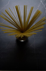 Italian pasta. Raw yellow spaghetti isolated in a transparent cup on a marble background. Like a plant. Focus at the top. Vertical view.