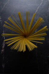 Italian pasta like a flower. Raw yellow spaghetti isolated in a transparent cup on a dark marble background. Focus in the center. Vertical view.