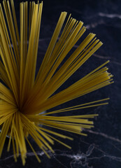 
Italian pasta is like a flower. cut raw yellow spaghetti isolated in a transparent cup on a dark marble background. Focus on the right side. Vertical view.