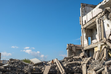 A ruined building with the remains of walls and a pile of concrete rubble against the background of the city and the blue sky. Background