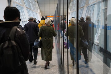 Almaty, Kazakhstan - 03.16.2022 : Passengers with luggage walk along the aisle to the airport building. Reflection in the glass.