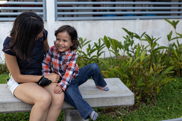 Mom and her Latin American son sitting on a bench showing their love with smiles and happiness....