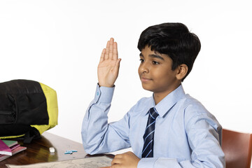 young boy from primary school studying seating hand raised in the classroom isolated on white background