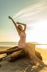Fototapeta na wymiar Carefree Bohemian girl sitting on driftwood at sunset