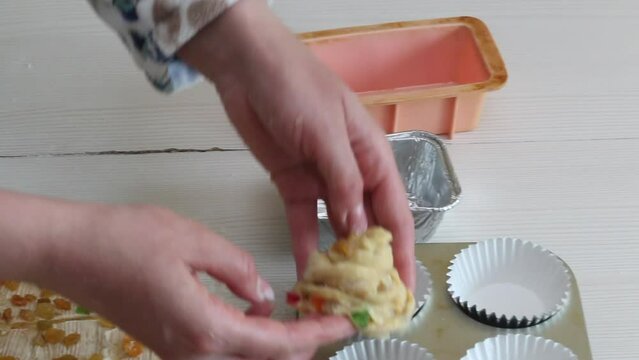 A woman prepares a cruffin with raisins and candied fruits. Rolled dough, tools and ingredients are laid out on the table. Close-up.