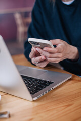 A young beautiful girl in a black jumper in a cafe works with a laptop and a phone