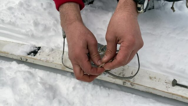 A man fixes a binding on a touring ski. Close-up of hands. Ski trip in the forests of Russia. Straight knot.