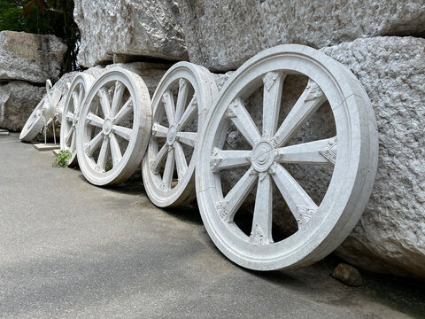 Wheel of Buddhist Dharma. Symbol of teaching in Buddhism. Wheels of white marble are set in a row, leaning to large boulders. Statue of  white stork in the background. Installation in Buddhist temple.