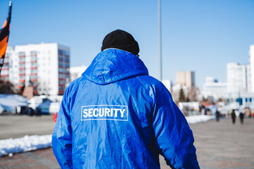 security. A guard in a blue uniform, a man standing with his back guarding the park area, a servant of the law, an inscription on the back of the guard.