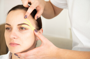 Close-up of cosmetologist making taping face procedure using yellow tapes. Anti-aging treatment against wrinkles.