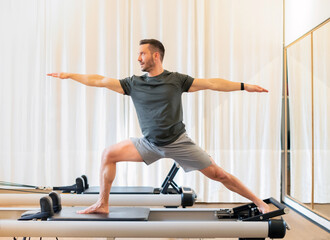 Man performing a Warrior 2 yoga pose on a pilates reformer bed