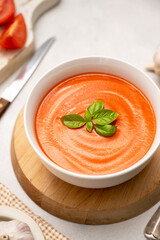 Tomato soup with fresh basil in white bowls. Bright background. Vegan creamy soup.