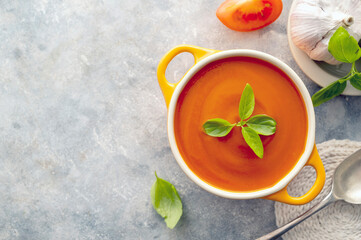 Tomato soup with fresh basil in orange bowl. Bright background. Healthy food concept. Copy space