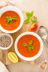 Tomato soup with fresh basil in white bowls. Served with sunflower seeds. Bright background. Top view, copy space.