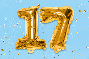 The number of the balloon made of golden foil, the number seventeen on a blue background with...