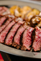 Marbled beef ribeye steak with grilled vegetable garnish, iron tray, wooden table. close up