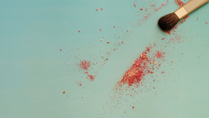 A cosmetic brush making a clear stroke path among some red cosmetic powder. On a greenish blue surface. With copy space on the left. 