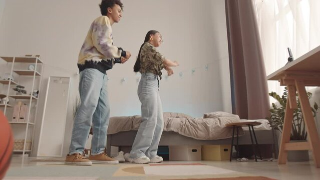 Full length slowmo of two diverse zoomer friends dancing together at home recording it on smartphone standing on tripod on desk
