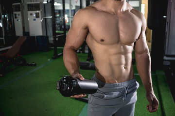 An anonymous muscular man shaking his protein drink. Post-workout beverage after working out at the gym.