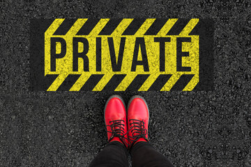 Word Private written on an asphalt road with legs and boots