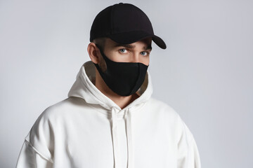 Man wearing white hoodie, black baseball cap and cloth face mask