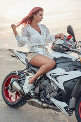 Obraz na płótnie Canvas Redhead female biker dressed in white attire and motorcycle