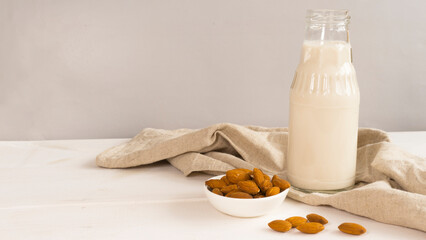 Bottle with almond milk and cup with almonds beside