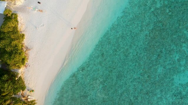 Beautiful beach with white sand and turquoise transparent sea water. Touristic vacation holidays destination. Tropical atoll island with coral reef in Maldives. Top down drone aerial video footage.