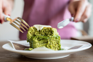 Someone taking a bite of Matcha scone with fork. Scones are small nibbles that are fairly plain on their own, but are classically eaten with jam and clotted cream. - obrazy, fototapety, plakaty